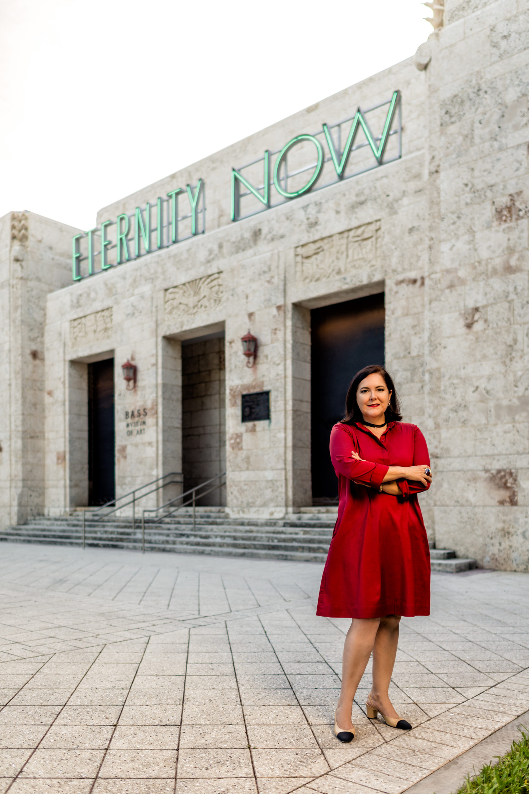 Full length image of Silvia Karman Cubina in a red knee length dress, standing in front of the Bass museum