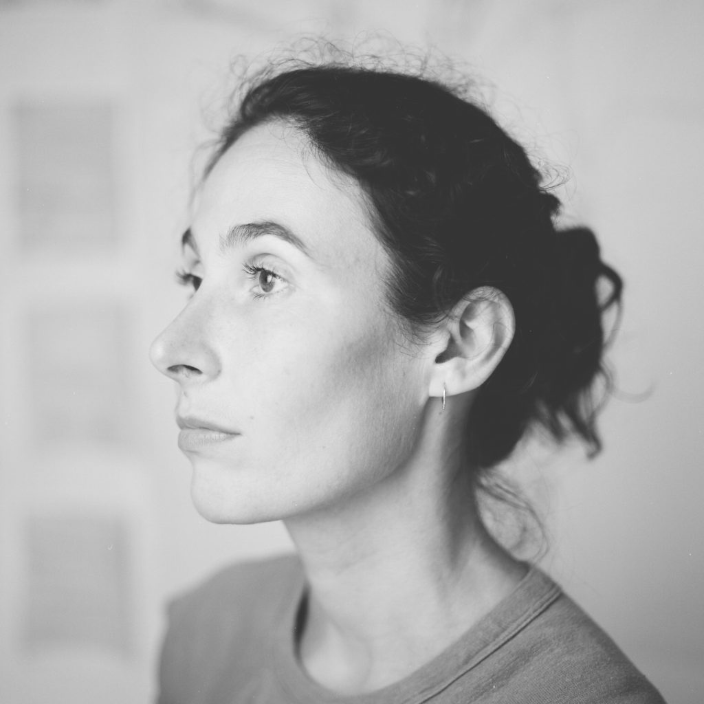 Headshot of Charlotte Caspers in black and white; white woman turned 3/4 profile to the left, dark hair pulled back in a low bun