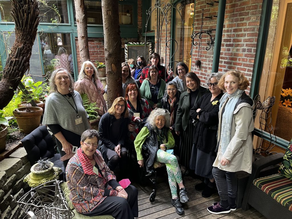 A group of women pose for a photo in a garden outside of a brick industrial-like building