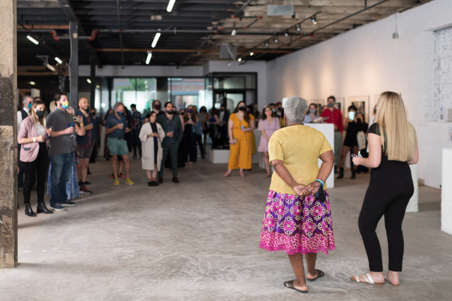 A group gathers in a semi-circle facing 2 women whose backs are to us