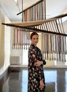 Eugenia Sucre stands in a gallery with a large art installation behind her