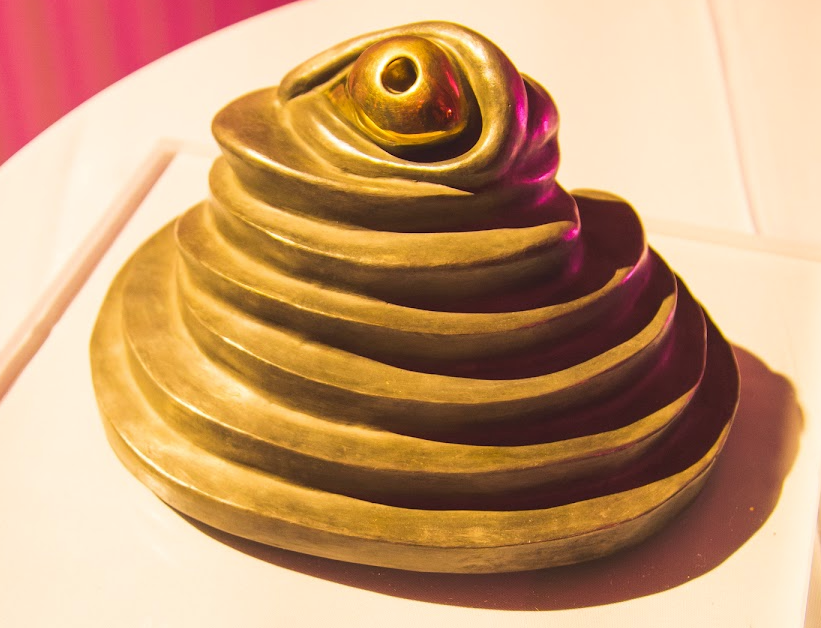 "Eye" sculpture by Louise Bourgeois. The sculpture is like a golden layered pyramid with an eyeball looking out and upwards from the top.