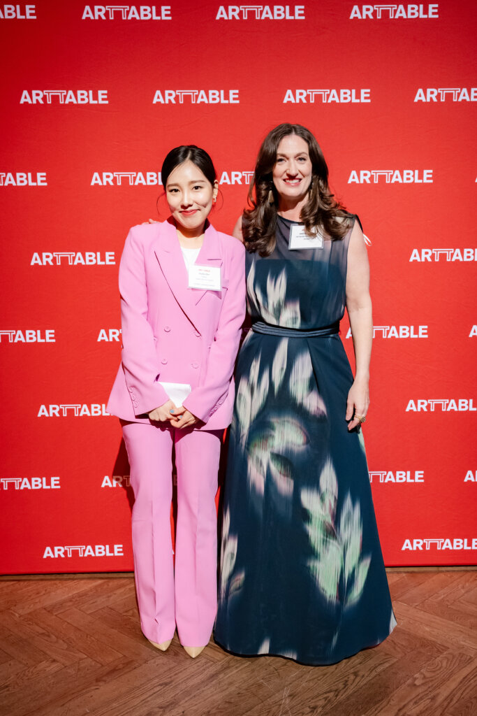 Soohyun (Sophie) Bae & Jessica L. Porter stand in front of a red ArtTable banner