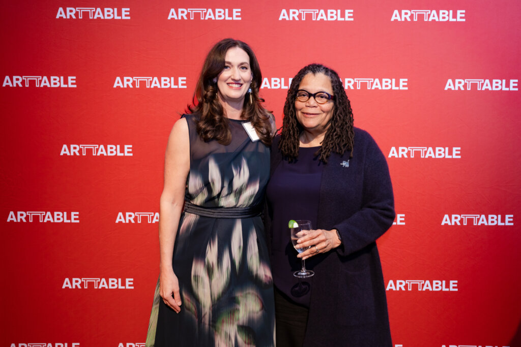 Two women standing in front of a red ArtTable banner