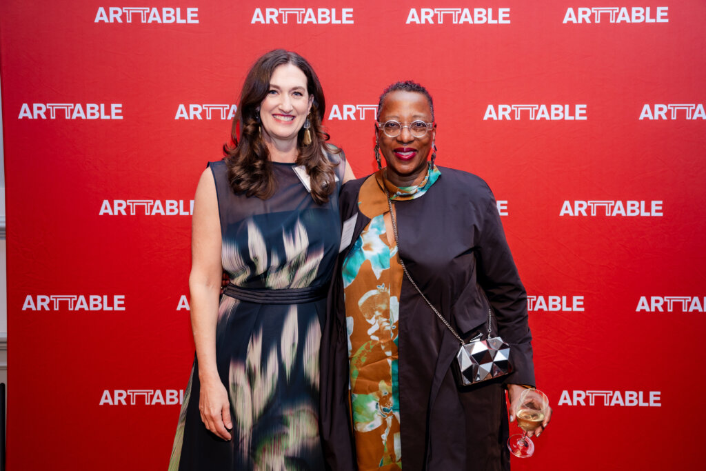 Two women standing in front of a red ArtTable banner