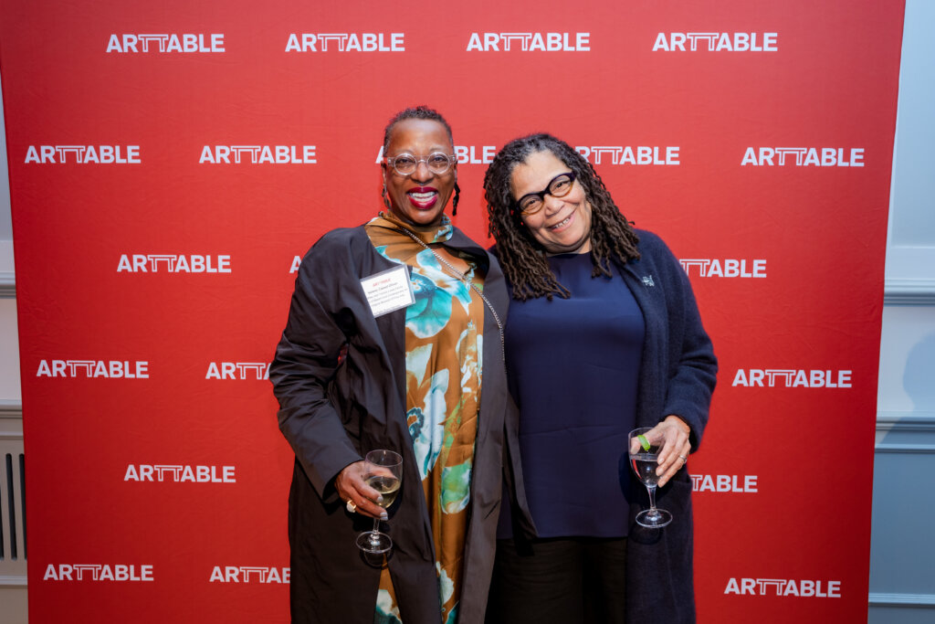 Two women standing in front of a red ArtTable banner
