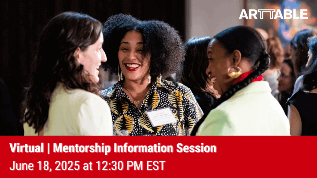 Picture of a woman with curly hair talking to 2 people facing away from the camera. They are all smiling.