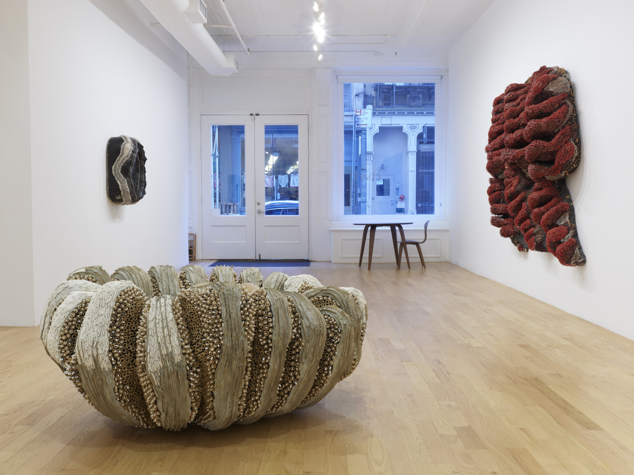 installation view of whitney oldenburg's ticket to paradise exhibition at CHART. It includes 3 sculptures. One small dark one on the far left wall. One large cream/tan one in the left center of the floor and one large red one on the right wall. All have an anemone look to them.