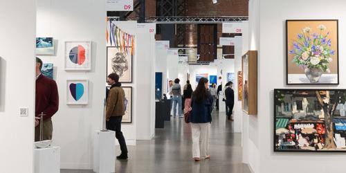 Busy white room in SoWa Power Station with people walking around booths looking at art at affordable art fair boston